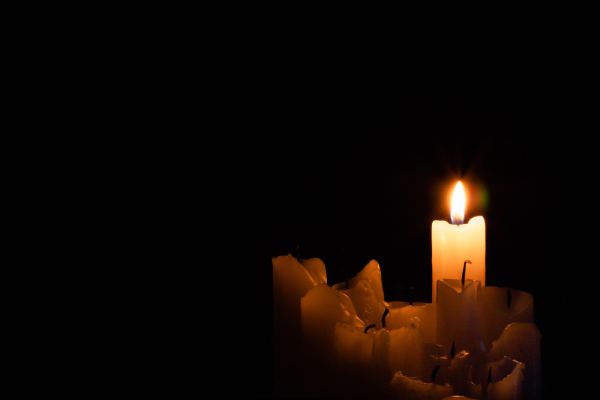 A group of burned out candles one still burning in the dark