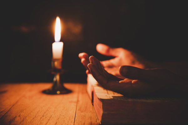 Close up man's hand is praying in the church with lit candle